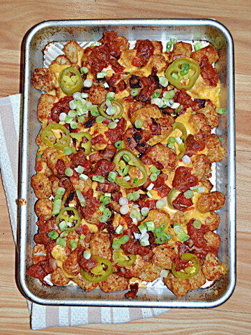 A pan of tater tots topped with salsa, cheese, jalapenos, and scallions.