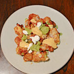 A plate with a pile of tater tots topped with cheese, jalapenos, sour cream, and salsa.