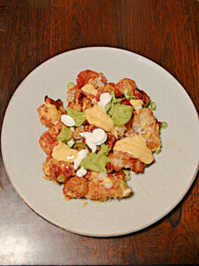 A plate with a pile of tater tots topped with cheese, jalapenos, sour cream, and salsa.