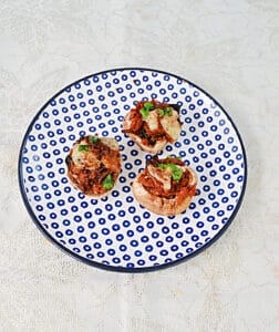 A small plate with three stuffed mushrooms topped with cheese and parsley.