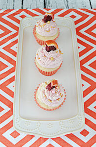 A white platter with three blood orange cupcakes each topped with a wedge of orange.