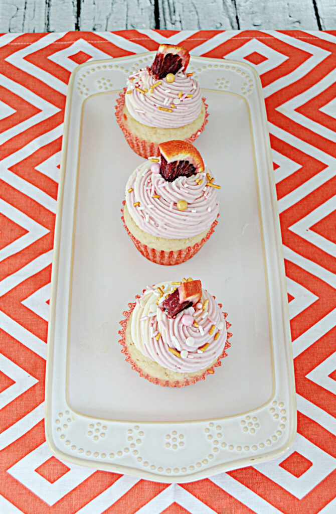 A white platter with three blood orange cupcakes each topped with a wedge of orange.