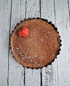 A chocolate crust filled with chocolate caramel filling with a strawberry on top.