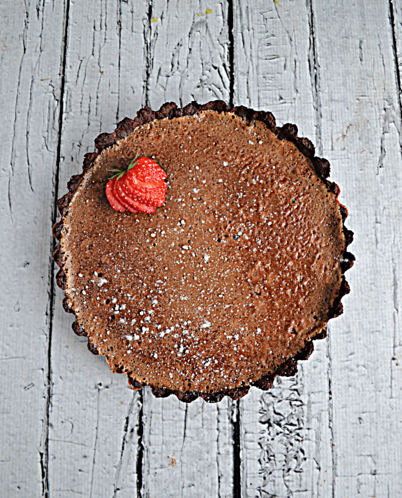 A chocolate crust filled with chocolate caramel filling with a strawberry on top. 
