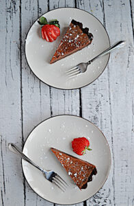 Two plates each one with a slice of Chocolate Caramel Tart, a fork on each plate, and a strawberry on each plate.
