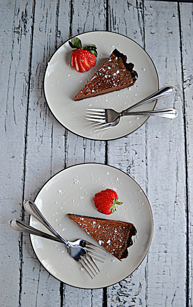 Two plates each one with a slice of Chocolate Caramel Tart, a fork on each plate, and a strawberry on each plate.