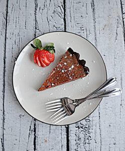 A plate with a slice of Chocolate Caramel Tart, two forks, and a cut strawberry.