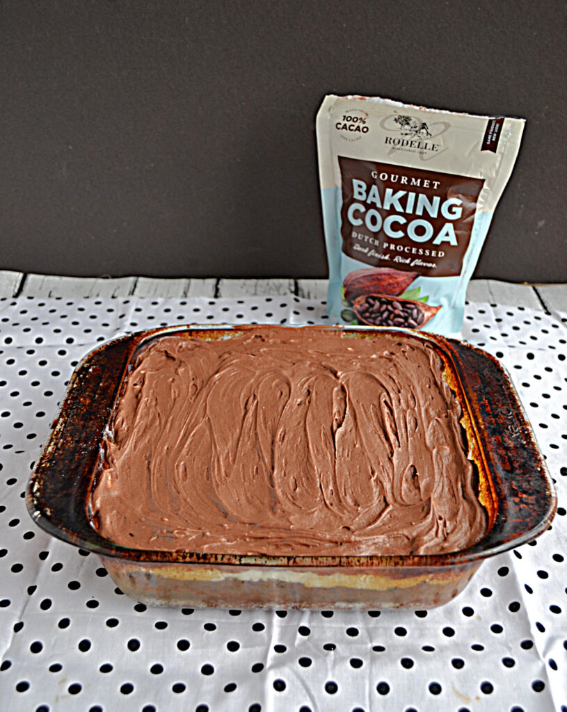 A pan of brownies with chocolate frosting on top and a bag of cocoa powder in the background.