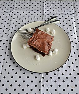 A plate with a chocolate frosted brownie on it, 2 forks, and a few mini marshmallows.