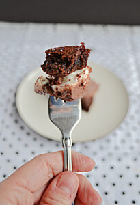 A close up view of a hand holding a fork with chocolate frosting, marshmallows, and a brownie on it.