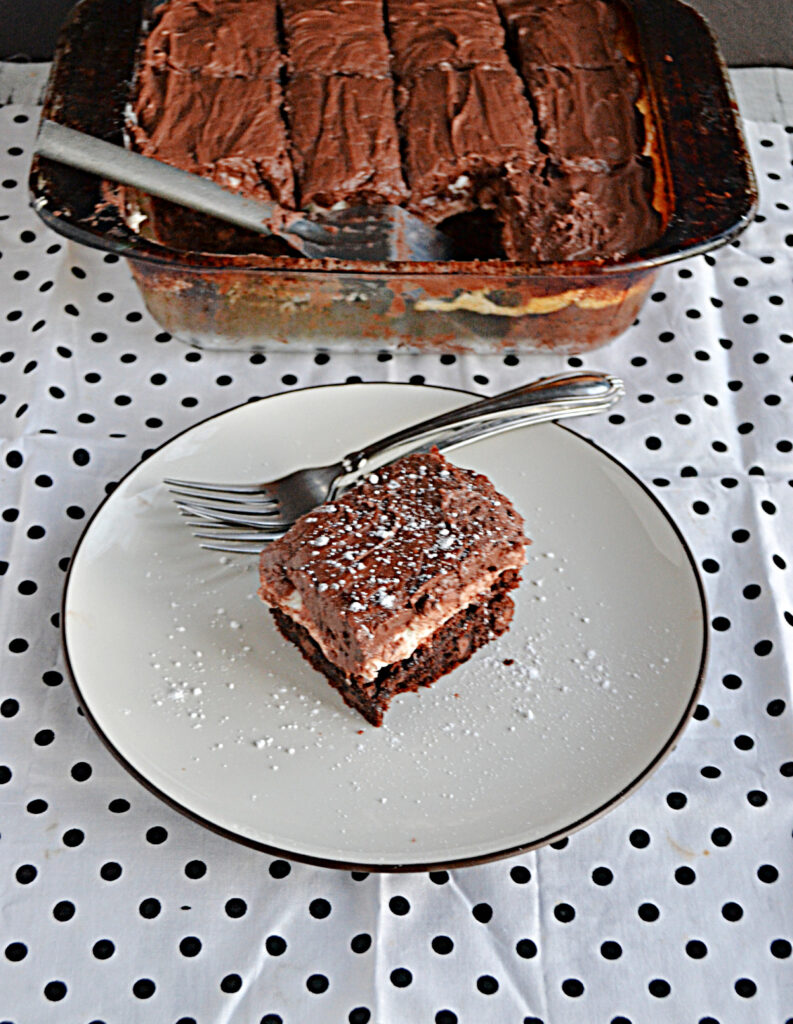 A plate with a marshmallow brownie covered in chocolate frosting and a fork on the plate with a pan of the brownies in the background. 