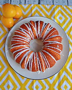 A Bundt Cake with a white glaze drizzled on it and a pile of lemons behind the cake.