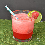 A glass of deep pink Raspberry Margaaritas with a straw in it and a lime slice and a raspberry on the rim.