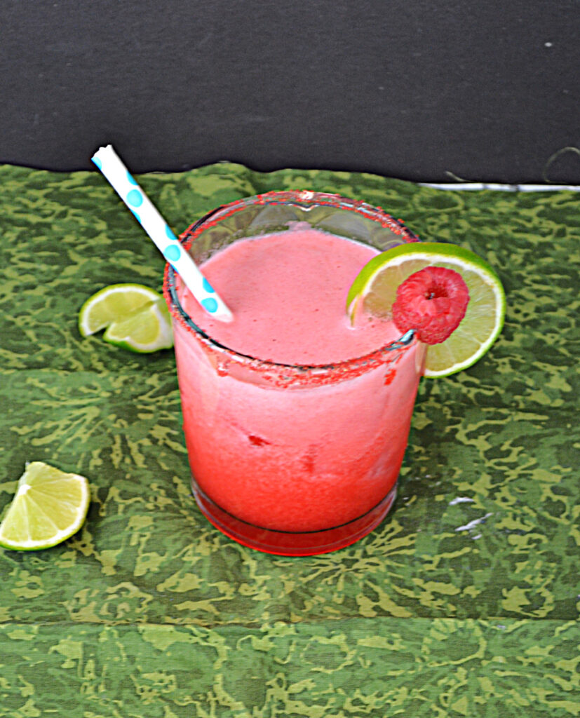 A top view of a pink Raspberry Margarita with a straw in it and a slice of lime and a raspberry on the rim with lime wedges around the glass.