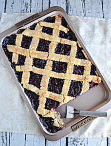 A jelly roll pan with a berry slab pie with lattice top and a spatula in the pan.