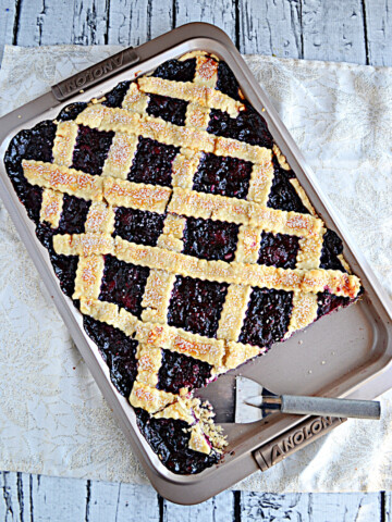 A jelly roll pan with a berry slab pie with lattice top and a spatula in the pan.