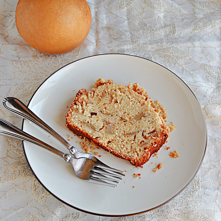A plate with a slice of caramelized Pear Bread and two forks on the plate with a pear behind the plate.
