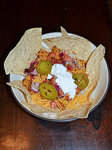 A bowl with chicken, cheese, jalapenos, and rice with tortilla chips around the edges.