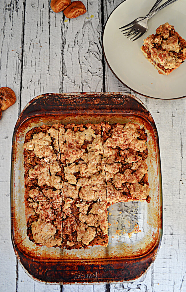 A baking dish with fig crumble bars in them with one piece missing and a plate with a crumble bar on it with 2 forks. 