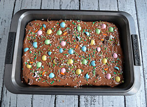 A pan of chocolate brownies with chocolate frosting and candy coated chocolate eggs on top.