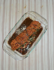 A baking dish with a pork loin inside tied with string and covered with balsamic.
