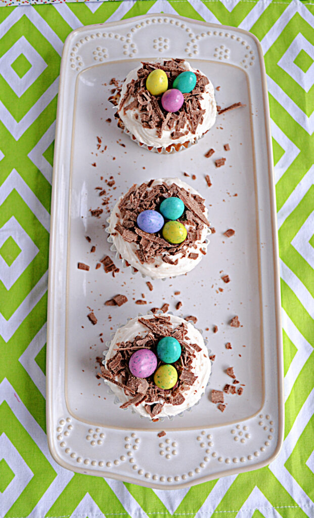 A white platter topped with three cupcakes with chocolate bird's nests and chocolate eggs on top. 