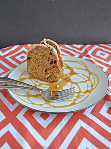 A side view of a plate drizzled with caramel, two forks, and a slice of carrot coffee cake on the plate.