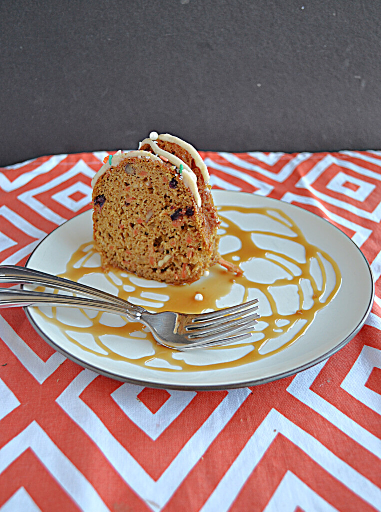 A side view of a plate drizzled with caramel, two forks, and a slice of carrot coffee cake on the plate.
