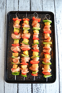 A pan with 4 chicken, bell pepper, and pineapple kabobs on it.