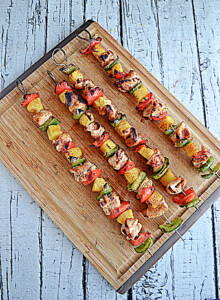 A cutting board with four grilled chicken, bell pepper, and pineapple kabobs on it.