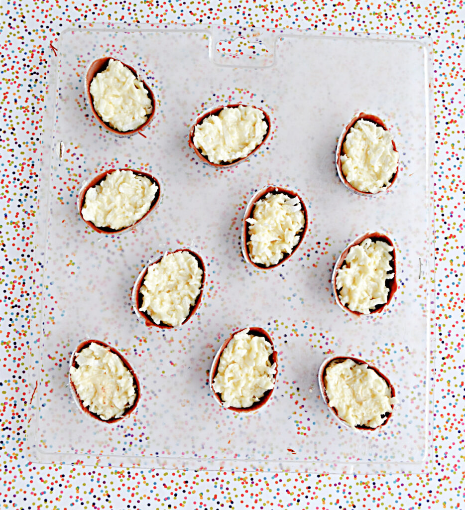 A candy egg mold with the chocolate and coconut filling in each egg.