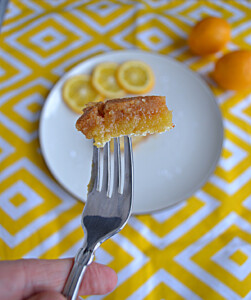 A close up view of a gluten free lemon bar on a fork with a plate with three lemon slices on it in the background.
