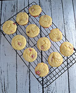 A cooling rack with a dozen lemon raspberry cupcakes on top.