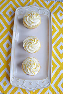 A white platter with three cupcakes topped with vanilla lemon frosting.