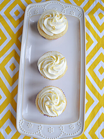 A white platter with three cupcakes topped with vanilla lemon frosting.