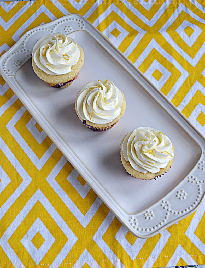 A white platter with three cupcakes topped with vanilla lemon frosting and fresh lemon zest.