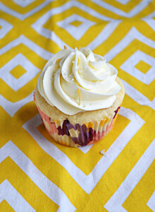 A close up view of a lemon raspberry cupcake with white frosting and lemon zest on top.