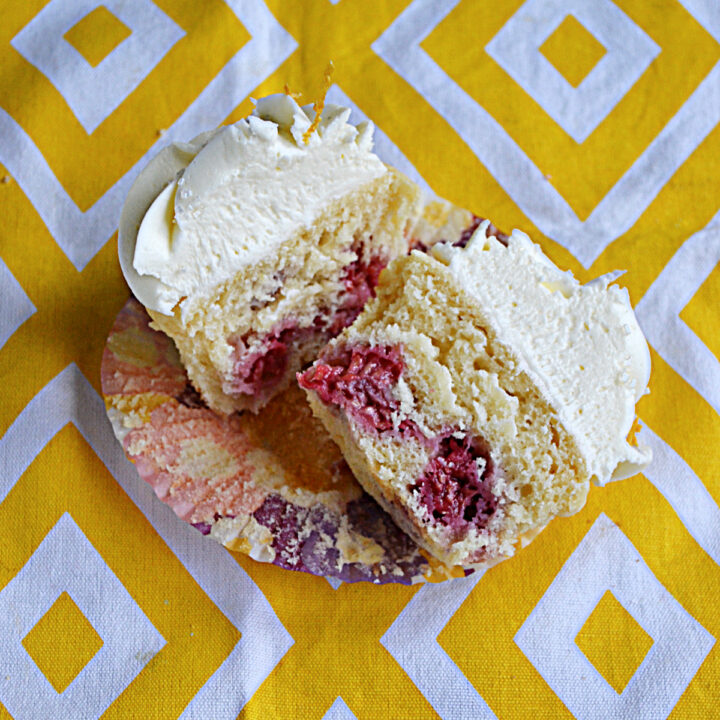 A cupcake cut in half with fresh raspberries showing inside.