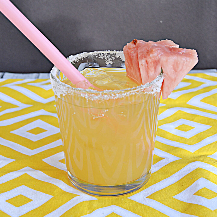 A yellow cocktail with a pink straw, sugar rim, and pink pineapple garnish.