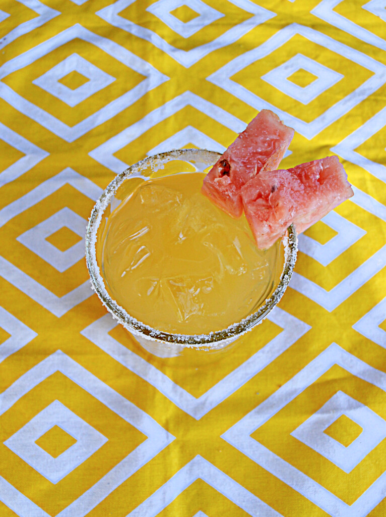 An overhead view of a yellow pineapple cocktail with pink pineapple rim. 
