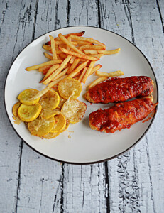A plate with buffalo chicken fingers, a pile of fries, and a scoop of baked yellow squash.