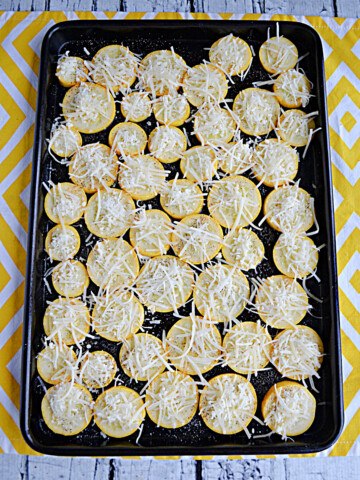A cookie sheet with yellow squash rounds topped with Parmesan cheese.