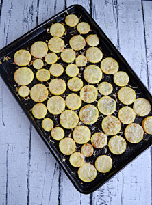 A baking sheet with roasted yellow squash rounds and melted Parmesan cheese on top.
