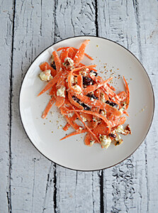 A plate with a carrot, pecan, and feta salad on it.