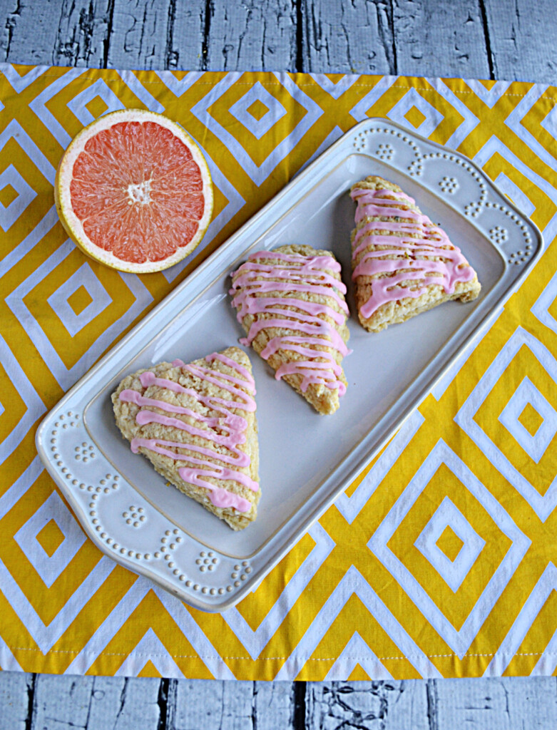 A platter of three grapefruit scones with pink glaze on top and half a grapefruit behind the platter. 