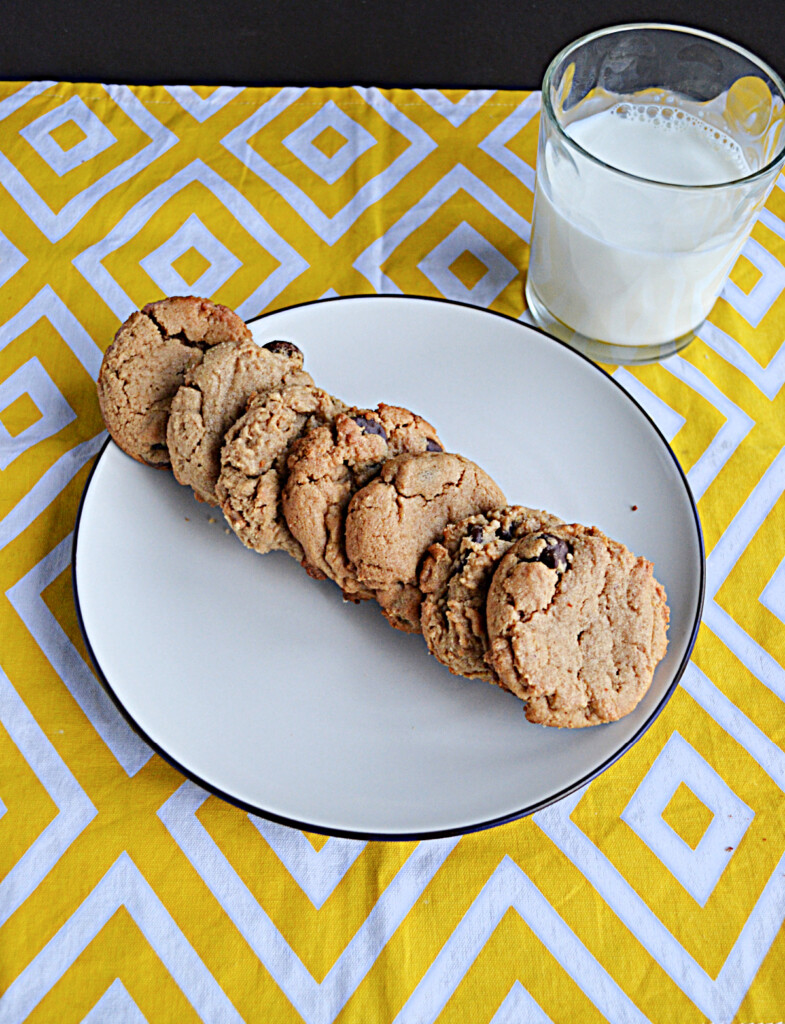 A plate with a row of cookies on it and a glass of milk behind. 