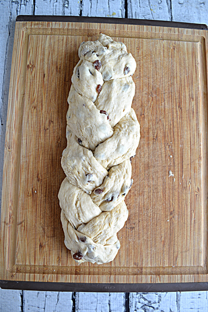 A cutting board with a loaf of braided Rum Raisin Bread waiting to be baked. 