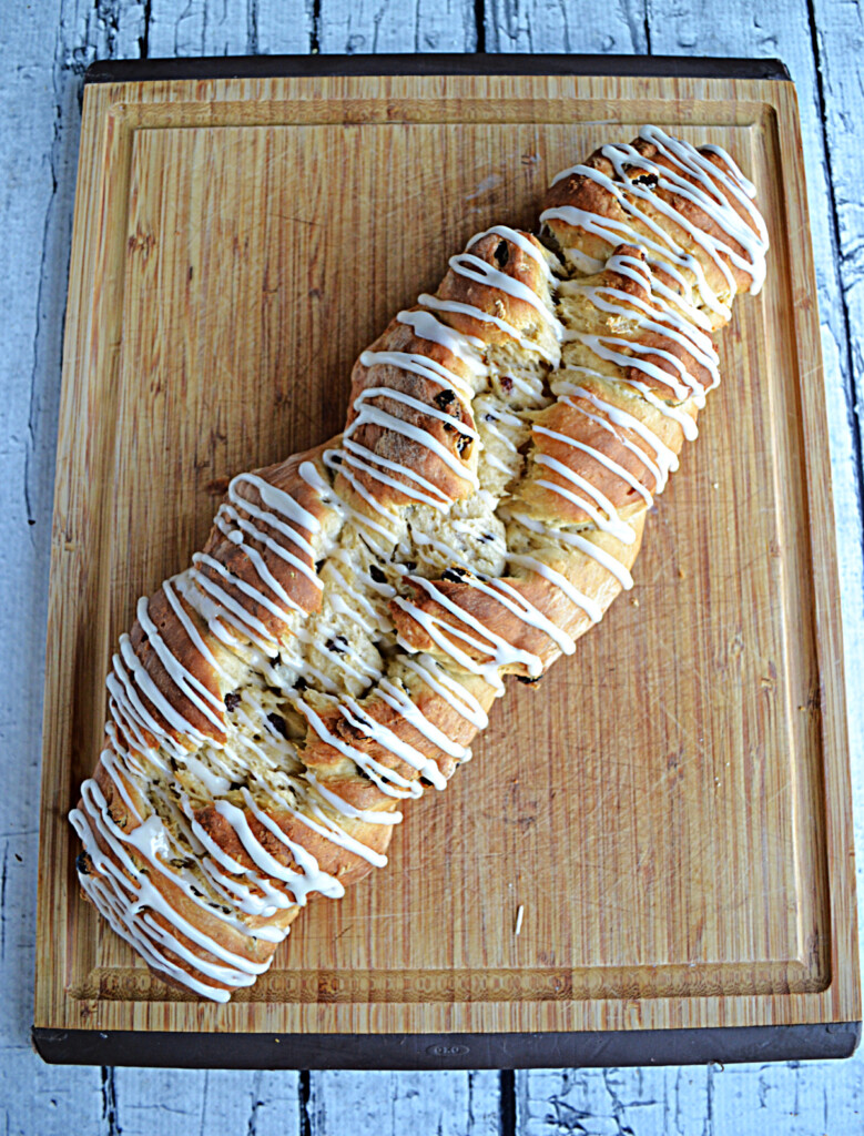 A cutting board with a golden brown loaf of Rum Raisin Bread with a sweet drizzle glaze.