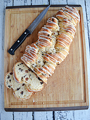 A cutting board with a golden brown loaf of Rum Raisin Bread with a glaze drizzled on top and two slices cut off them bread.