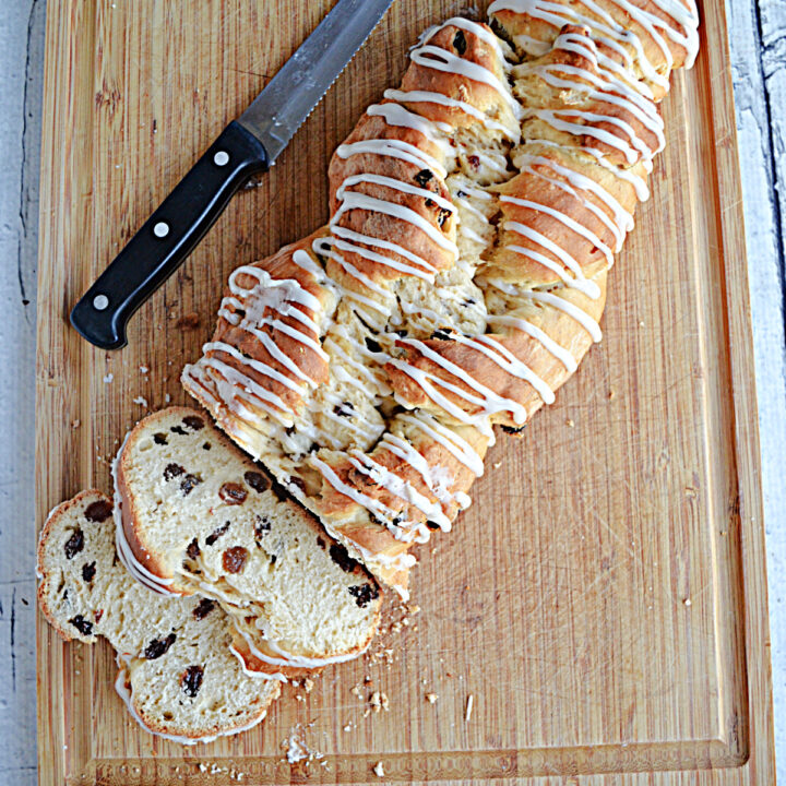 A cutting board with a golden brown loaf of Rum Raisin Bread with a glaze drizzled on top and two slices cut off them bread.